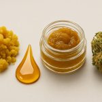 various cannabis concentrates including a jar of extract, a pile of crumble, and a flower bud on a neutral background